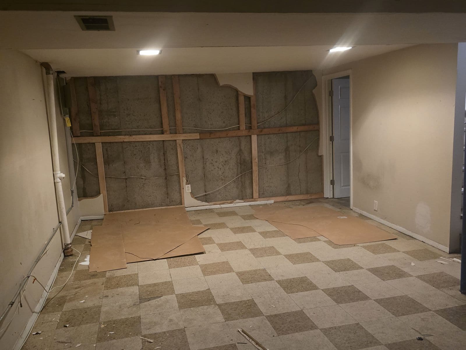 Basement before renovation — checkered tile floor, walls opened to the framing