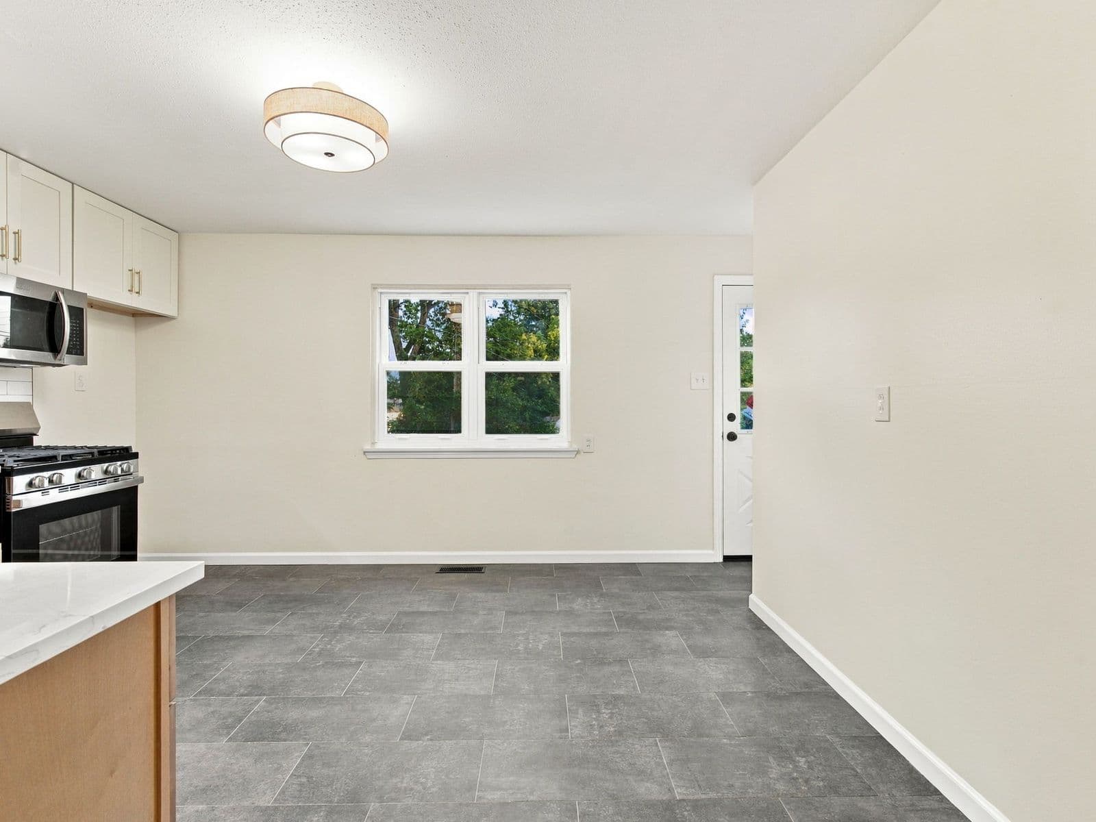 The same kitchen after — white upper cabinets, stainless range and microwave, gray tile floor, fresh paint
