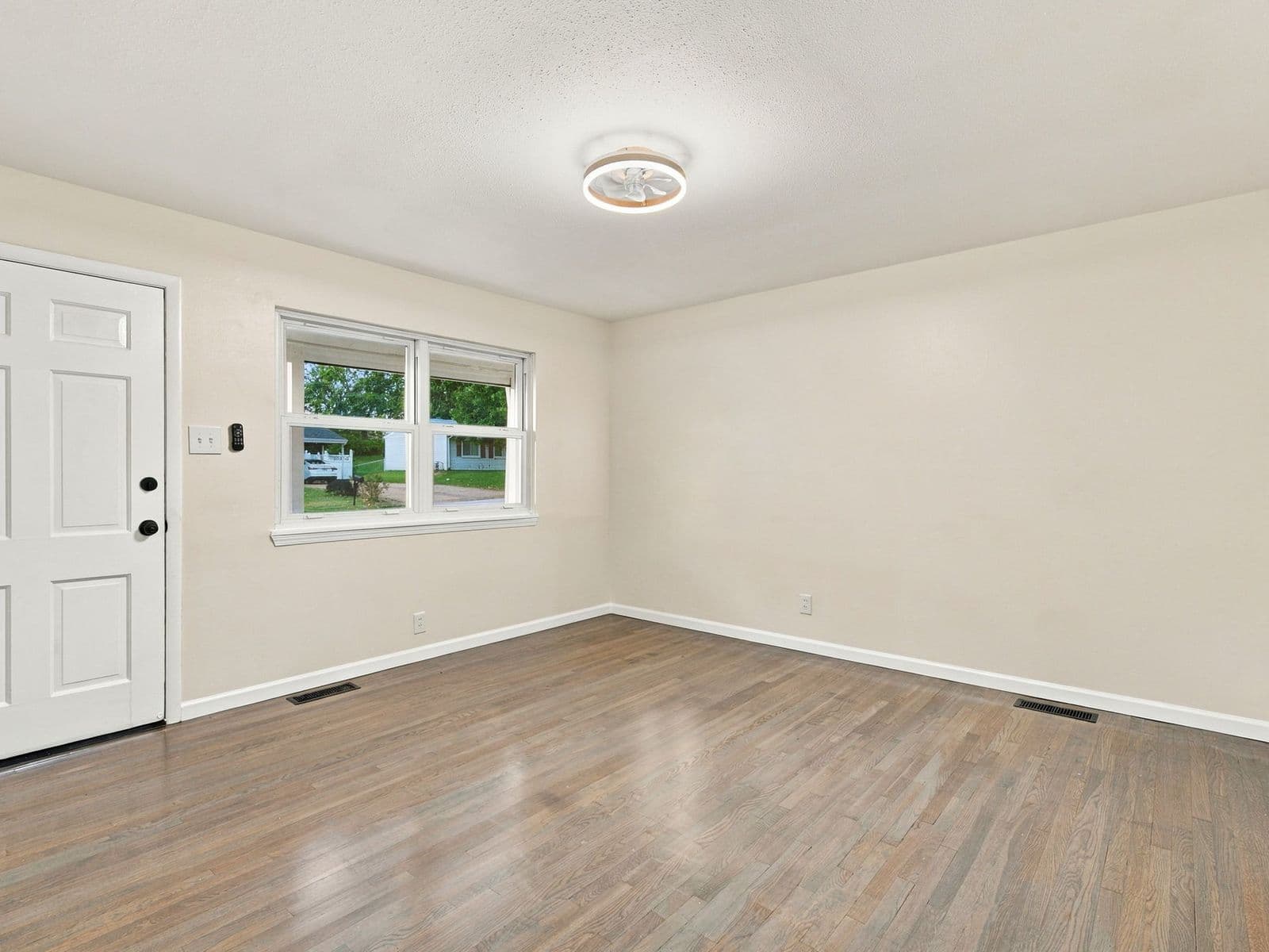 The same living room after — fresh walls and trim, refinished wood floor, new light fixture