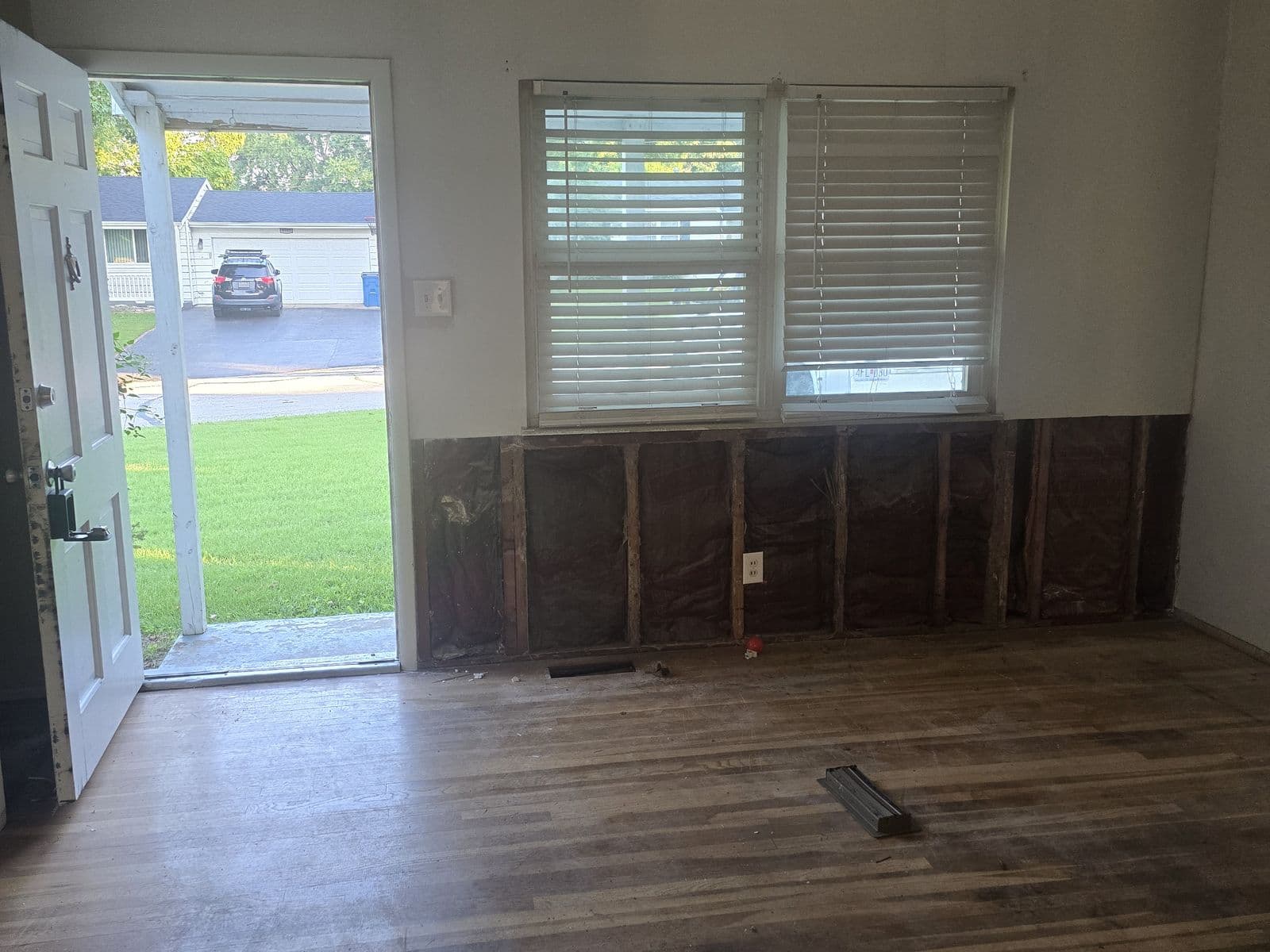 Living room before renovation — paneling torn off the lower walls, worn wood floor, old ceiling fan