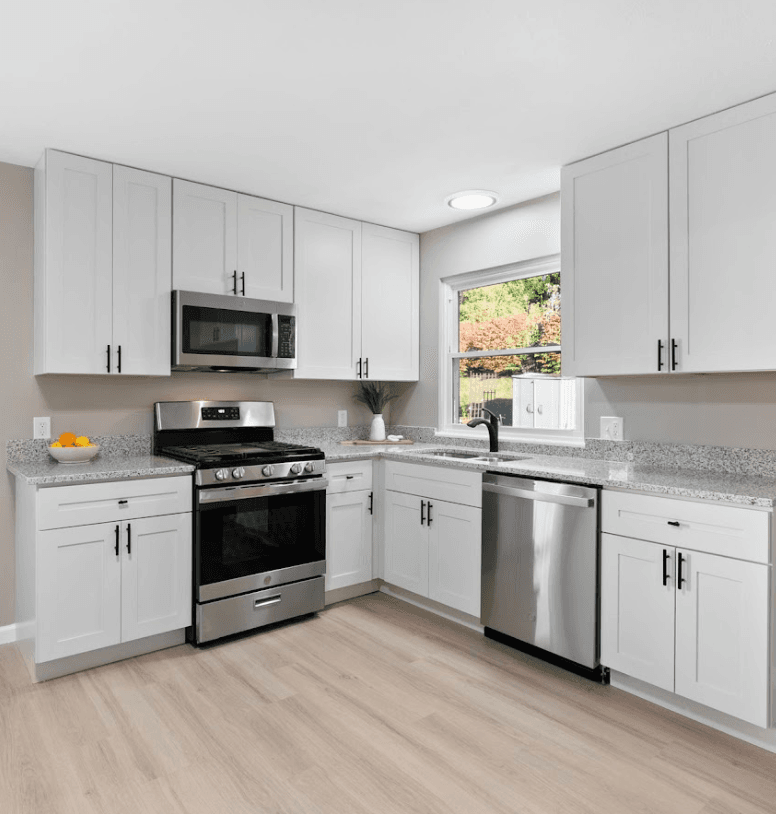 Kitchen after — bright white shaker cabinets, granite, stainless steel