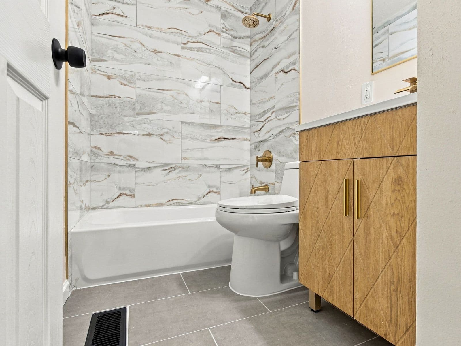 The same bathroom after — marble-look tile tub surround, wood vanity, new toilet, tile floor