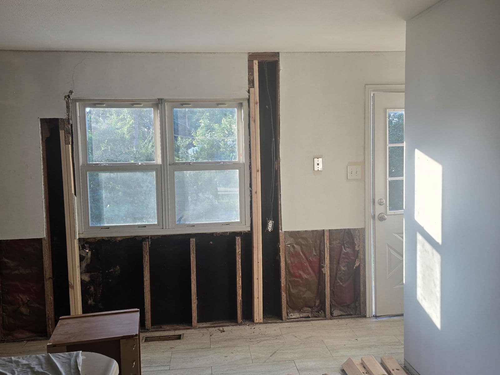 Kitchen before renovation — paneling torn out to the studs, cabinets removed, old tile floor